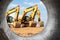 Several powerful excavators at the construction site. View of the excavator through the pipe. Close-up of earthmoving machinery.