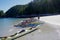 Several sea kayaks beached on white sand, green forest in the background
