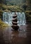 Several stones arranged in the river with the background of a waterfall