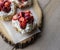 Several strawberry shortcakes with fresh whipped cream on parchment paper and wood trivet.