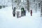 Several of unrecognizable little kids with teachers of kindergarten, back to us, walk holding hands in snowy park