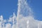 Several vertical streams of water rise up and splatter against the blue cloudy summer sky.