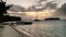 Several vessels docked against the shoreline near a picturesque beach at sunset.