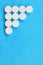 Several white tablets lie on a bright blue background in the form of a triangular arrow. Background image on medicine and