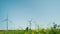 Several wind turbines. In the foreground there is a green grass, in the background a plane is flying in the sky