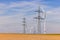Several wind turbines and power poles on a field under blue sky