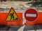 Several yellow plastic roadblocks stand against the background of forbidding signs to restrict traffic and road works