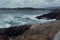 Severe gloomy norway landscape with stormy sea - grey waves of Arctic Ocean in gale and black granite rocks in cloudy weather.