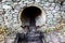 Sewage pipe with water and stonework behind metal mesh. Part of reinforced soil wall in park. Large gray stones