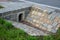 Sewer bridge through a ditch by the road. concrete hole with surroundings of stone paving. grassy slope by the road. has the task