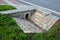 Sewer bridge through a ditch by the road. concrete hole with surroundings of stone paving. grassy slope by the road. has the task