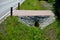 Sewer bridge through a ditch by the road. concrete hole with surroundings of stone paving. grassy slope by the road. has the task