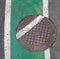 Sewer metal cap on teh green painted bicycle lane on the road.
