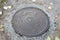 Sewer, plumbing, cable hatch made of cast iron on a background of rough concrete with autumn leaves.