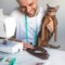 Sewing clothes for pets. Tailoring clothes for cats. A laughing tailor in white t-shirt is sewing clothes for his abyssinian cat.