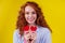 Sex education concept.redhaired ginger curly woman holding heart paper valentites card in studio yellow background