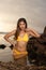 Sexy Asian woman spending sunset on the beach. Attractive woman wearing yellow bikini. Slim fit body. Tanned skin. Ocean water.