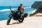 Sexy athletic man with perfect naked body sitting on motorbike, ocean waves and beautiful mountains on background