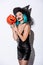 Sexy girl in black witch Halloween costume with blue hair holding spooky carved pumpkin on white background