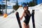 Sexy skier woman in black swimsuit with skis on background of mountains resort on sunny winter day.