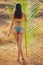 Sexy slender long leggy brunett photo model on the beach with palms and blue sky.woman in a green swimsuit posing in a