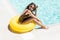 Sexy sporty woman in sensual bikini swimsuit, sunglasses and big yellow inflatable ring sit on the edge of the pool at hotel