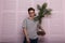 Sexy stylish young man hipster in a fashionable T-shirt in vintage glasses poses with an exotic artificial flower in a glass pot