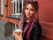 Sexy woman with big brown eyes and hairstyle with pink dreadlocks and pigtails in black clothes is holding coffee. Shot outdoors