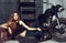 Sexy woman model in erotic leather jacket lying in dirty, rubber tire on floor on motorcycle garage background. Wheel
