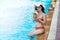 Sexy young asian woman in swimsuits in summer. beautiful woman in orange bikini with hat sitting in swimming pool with tropical