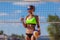 Sexy young athletic girl drinking water from a plastic bottle after playing beach volleyball while standing with a ball