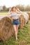 Sexy young blonde girl on haystack roll on harvested wheat field in the summer. Selective focus. full body fashion