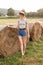 Sexy young blonde girl on haystack roll on harvested wheat field in the summer. Selective focus. full body fashion portrait of