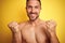 Sexy young shirtless man showing nude fitness chest over yellow isolated background celebrating surprised and amazed for success