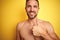 Sexy young shirtless man showing nude fitness chest over yellow isolated background doing happy thumbs up gesture with hand