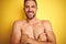 Sexy young shirtless man showing nude fitness chest over yellow isolated background happy face smiling with crossed arms looking