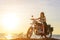 A sexy young woman in sunglasses sits on a black chrome motorbike. Hipster girl on a motorcycle against the sunset