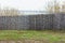 Shabby fence in the sunny spring day. Background texture of old grey wooden fence from whole logs with  knots