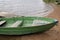 Shabby wooden boat painted green with two benches for rowing moored by rope at small board pier on shore of a bay of lake