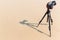 Shadow of photo camera on tripod. The shoot process on sand beach background. Shadow of a camera on the sand with a tripod shadow