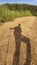 Shadow silhouette of male hiker walking on dirt road with stick in hand