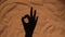 Shadow of a woman's hand on sand of beach showing ok sign. Close up silhouette of a female hand. Summer holiday by