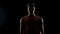 Shadowed topless man standing against black background, hopelessness concept