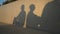 Shadows of argued couple sitting back to back as male silhouette passing and woman leaving man. Unrecognizable boyfriend