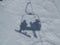 Shadows of a snowboarder and skier riding a chair lift