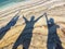 Shadows of three happy people at beach raising hands