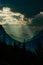 Shafts of light break through the stormy clouds onto the steep mountain valley slope, silhouetting trees in the foreground