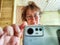 A shaggy, funny middle-aged woman in glasses takes a selfie on her smartphone in front of the mirror in the morning. A