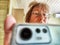 A shaggy, funny middle-aged woman in glasses takes a selfie on her smartphone in front of the mirror in the morning. A