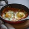 Shakshouka with avocado in a frying pan on a gray table close-up